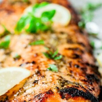 Close-up of a lemon pepper salmon fillet garnished with fresh basil and lemon slices, served on a light surface.