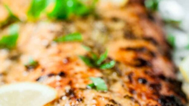 Close-up of a lemon pepper salmon fillet garnished with fresh basil and lemon slices, served on a light surface.