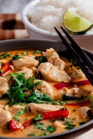 Thai Chicken Coconut Curry in a bowl with chopsticks, rice, and lime slices.