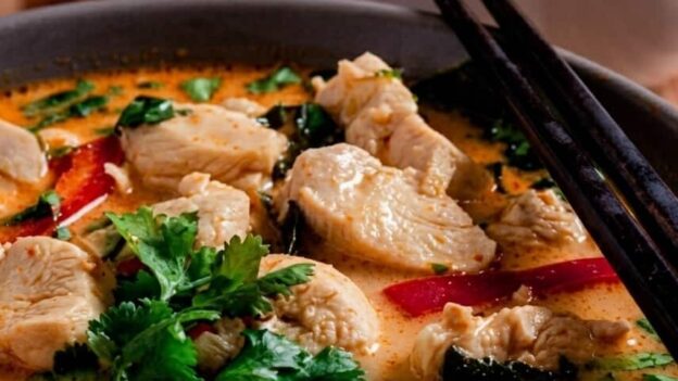 Thai Chicken Coconut Curry in a bowl with chopsticks, rice, and lime slices.