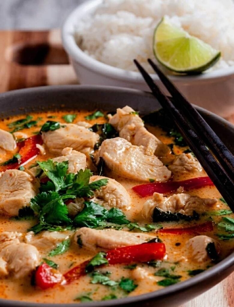 Thai Chicken Coconut Curry in a bowl with chopsticks, rice, and lime slices. 