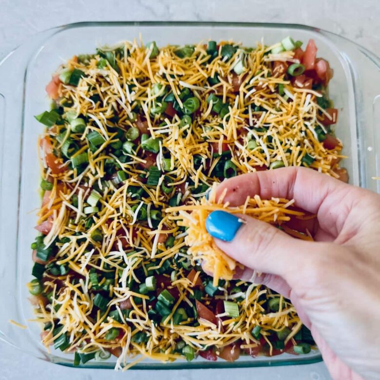 7 layer mexican dip having shredded cheese sprinkled on top, getting ready to be served.