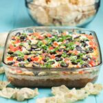Side shot of 7 layer mexican dip with tortilla scoop chips on the side.