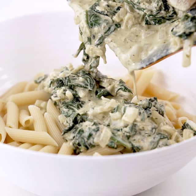 Chicken florentine pasta sauce being added to cooked pasta.