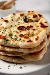 Garlic naan bread stacked one on top of another, brushed with garlic butter and fresh parsley garnished on top.