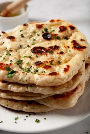 Garlic naan bread stacked one on top of another, brushed with garlic butter and fresh parsley garnished on top.