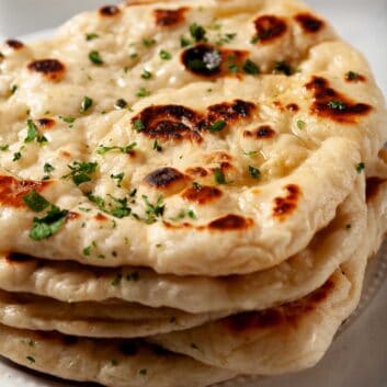 Garlic naan bread stacked one on top of another, brushed with garlic butter and fresh parsley garnished on top.