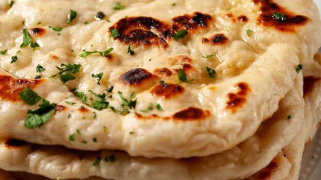 Garlic naan bread stacked one on top of another, brushed with garlic butter and fresh parsley garnished on top.