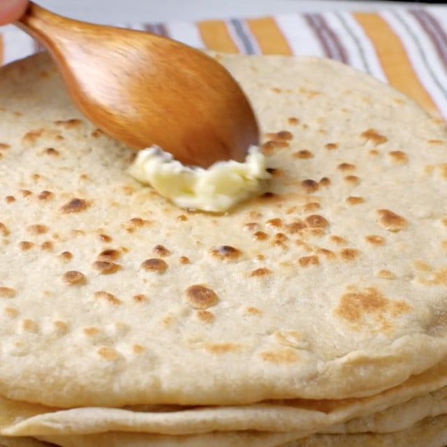 Garlic naan being brushed with butter being serving.