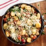 Overhead shot of a bowl of gnocchi with sausage topped with cheese and fresh herbs.