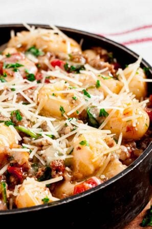 Closeup shot of a bowl of gnocchi with sausage topped with cheese and fresh herbs.