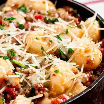 Closeup shot of a bowl of gnocchi with sausage topped with cheese and fresh herbs.