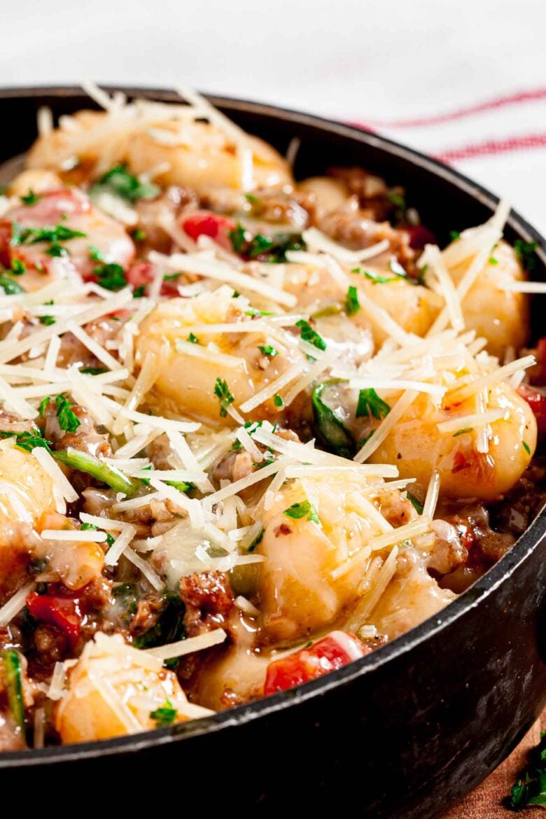 Closeup shot of a bowl of gnocchi with sausage topped with cheese and fresh herbs.