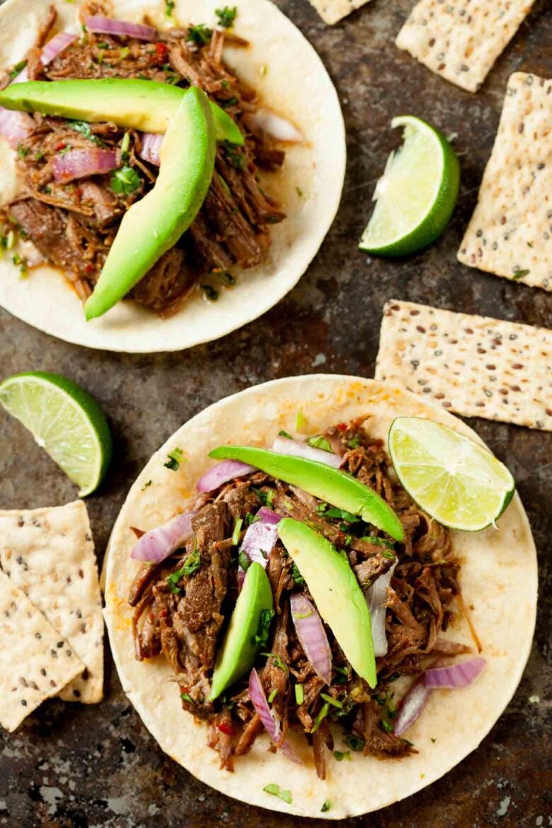 Overhead shot of instant pot beef barbacao tacos with lime and avocados.
