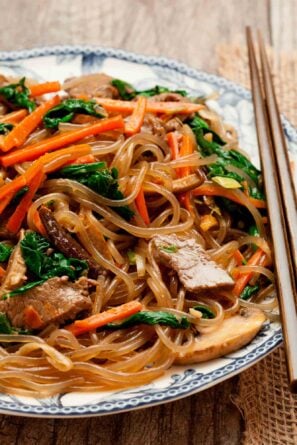 Closeup shot of japchae served in a bowl with chopsticks on the side.