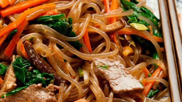 Closeup shot of japchae served in a bowl with chopsticks on the side.