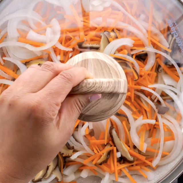 Japechae vegetables being cooked with a lid on the pan.