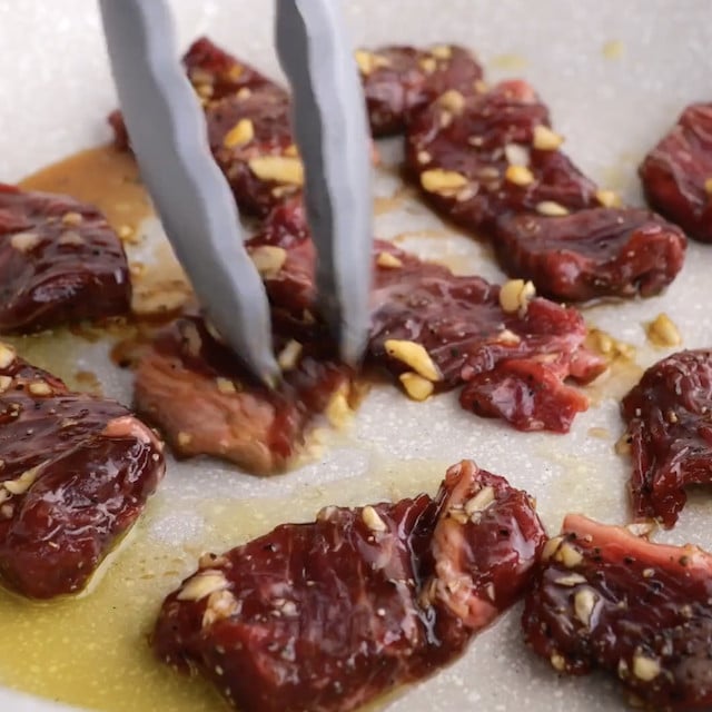Thinly sliced ribeye beef being sautéed in a skillet for Korean Japchae recipe.