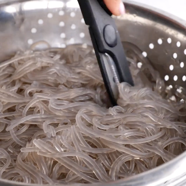 Japchae noodles being cut with kitchen scissors.