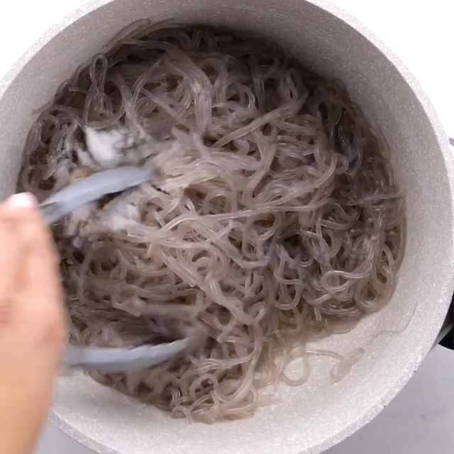 Japchae noodles being tossed with seasonings and sauces.