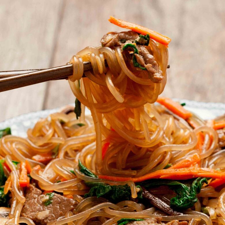 Closeup shot of chopsticks holding japchae noodles.