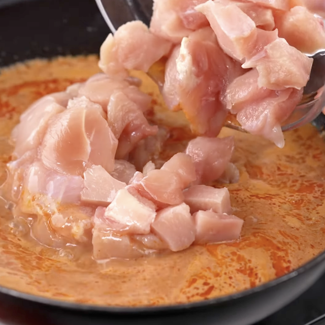 Chicken being added to pot with thai curry to make Thai curry noodles.