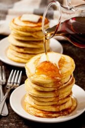 Syrup being poured over a stack of freshly made fluffy buttermilk pancakes.