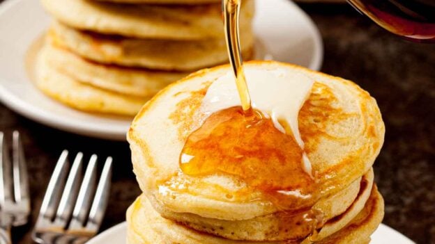 Syrup being poured over a stack of freshly made fluffy buttermilk pancakes.