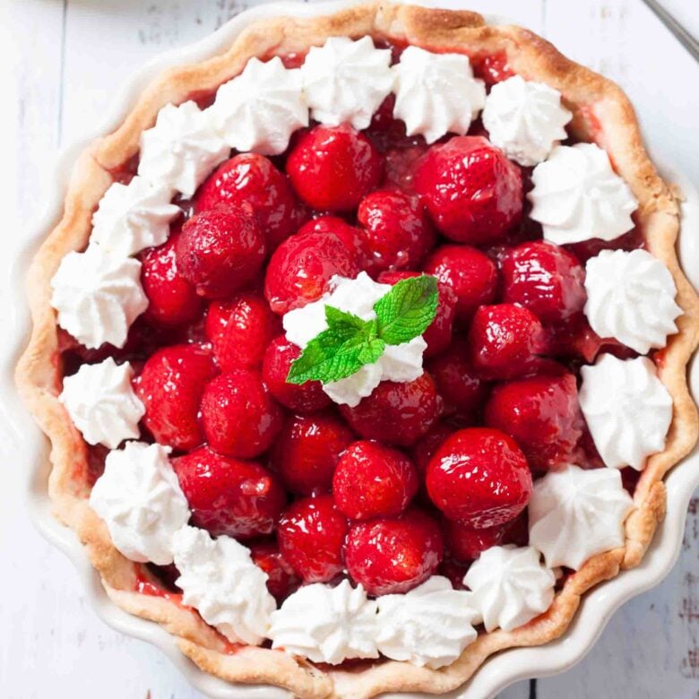 Fresh strawberry pie with whole glazed berries and piped whipped cream in a flaky butter crust. 