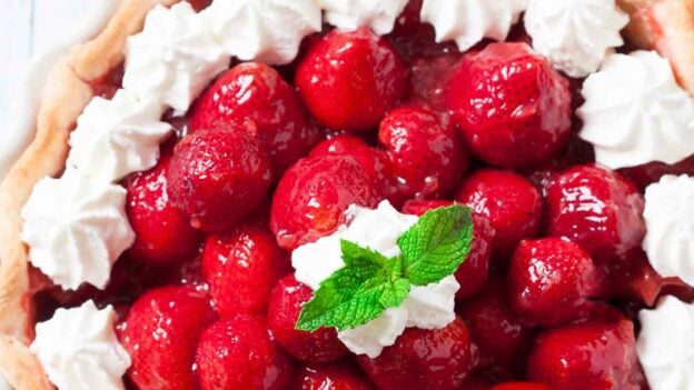 Overhead shot of a fresh strawberry pie with piped whipped cream.