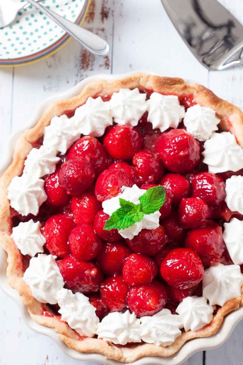 Fresh strawberry pie with a glossy berry filling and piped whipped cream in a flaky butter crust.