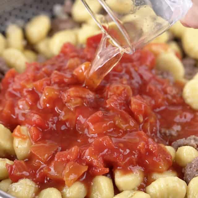 Broth being added to a pot with gnocchi and tomatoes to make gnocchi with sausage.