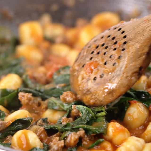 Spinach being stirred into gnocchi with sausage.