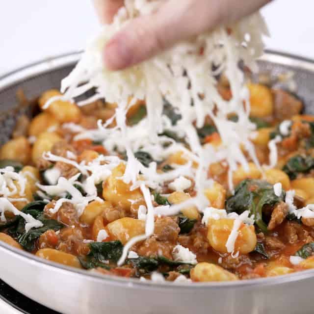 Gnocchi with sausage being topped with cheese before serving.