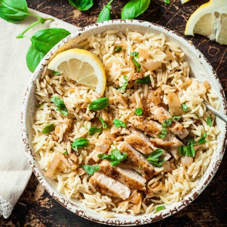 Overhead shot of lemon chicken orzo with lemon slice and herbs on top.