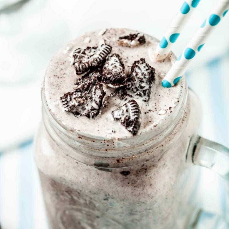 Close up of Blizzard Oreo Dessert in a clear mug with handle with two white and green straws coming out of the drink.