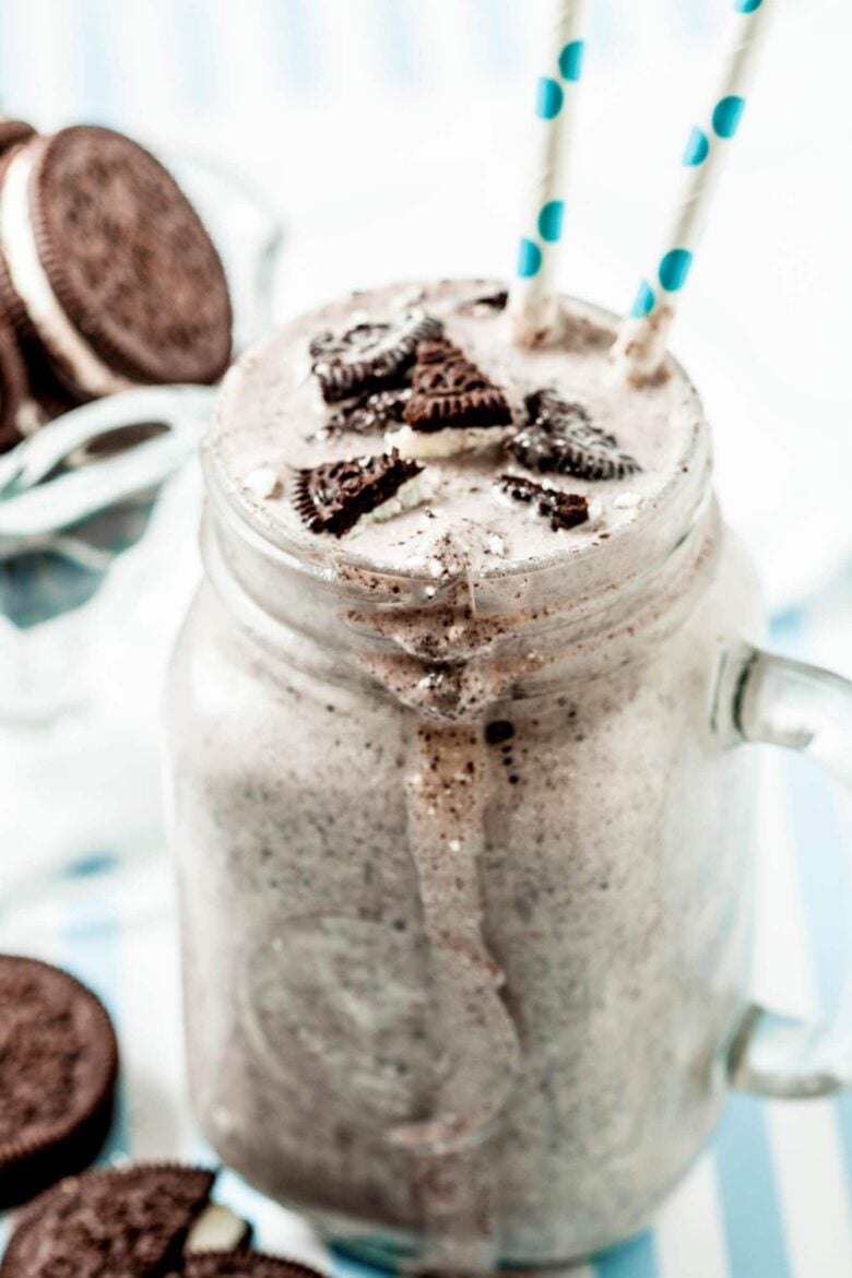 Blizzard recipe in a clear mason jar mug, with a handle with two straws as well as crushed cookies added as the topping.