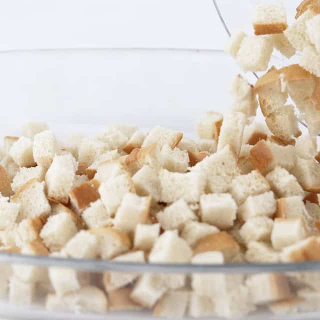 Bread cubes being added to a baking dish to make blueberry french toast casserole.