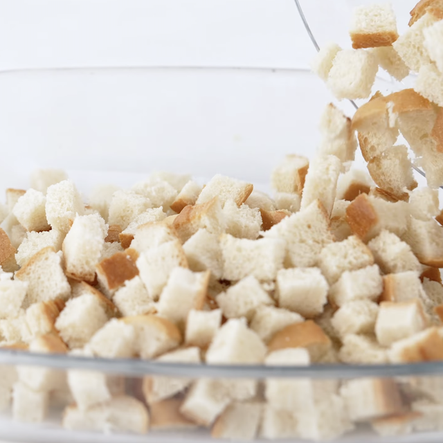 Bread cubes being added to a baking dish to make blueberry french toast casserole.