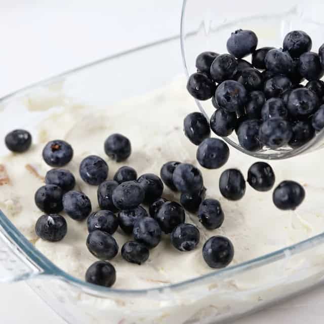 Blueberries being added to a casserole to make blueberry french toast casserole.