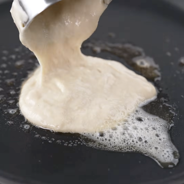 Pancake batter being poured onto a hot skillet.