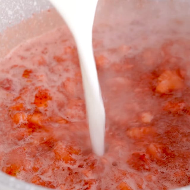 Dissolved cornstarch slurry being added to a pot with strawberry filling.