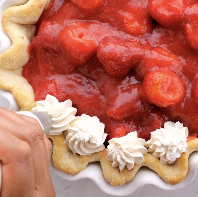 Stabilized whipped cream being piped onto a fresh strawberry pie.