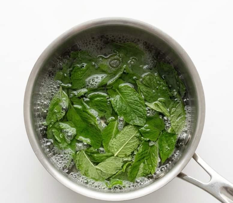 Small pot boiling on the stove with the water, sugar, and mint leaves.