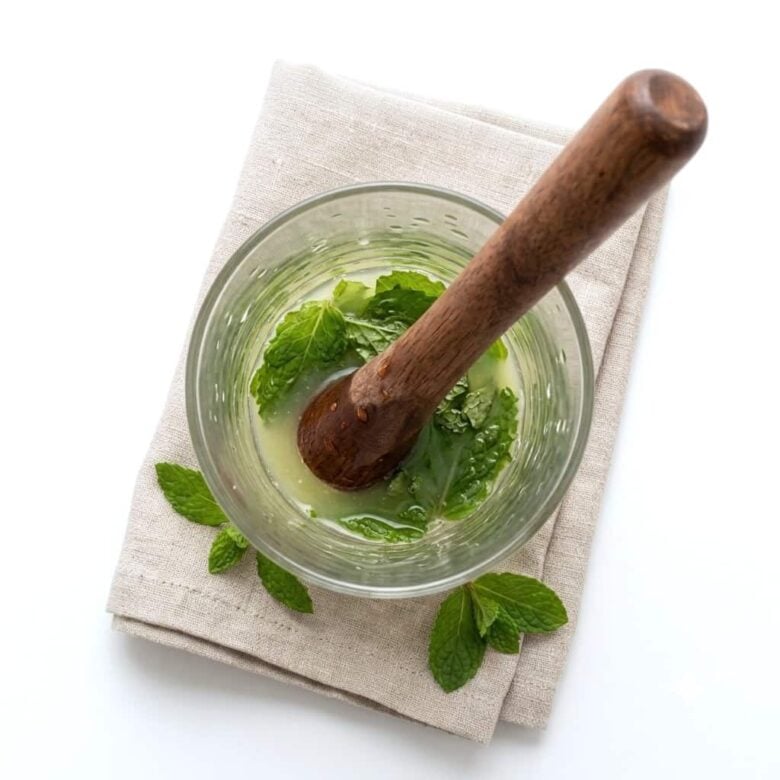 Muddling the mint leaves in the highball glass.