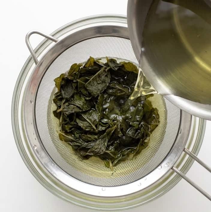 Pouring the mojito syrup mixture through a mesh strainer to strain out any mint leaves.
