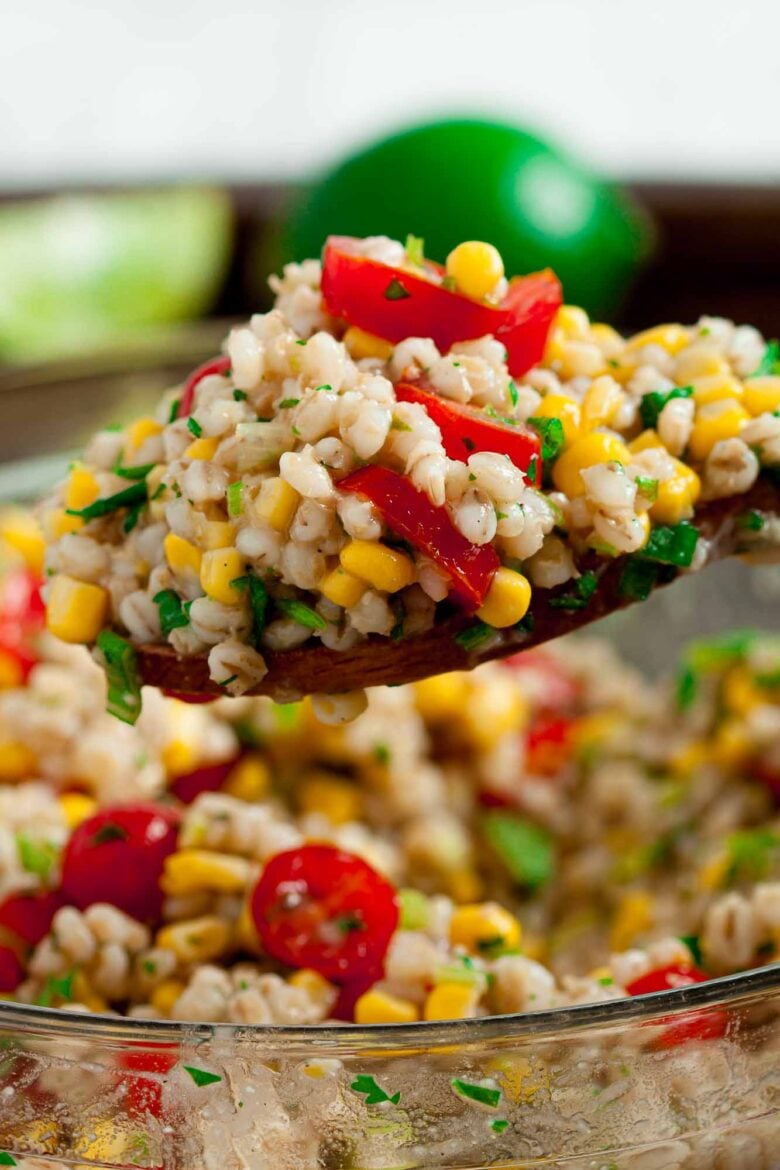Close up of Barley Salad on a spoon with a clear bowl full in the background. 