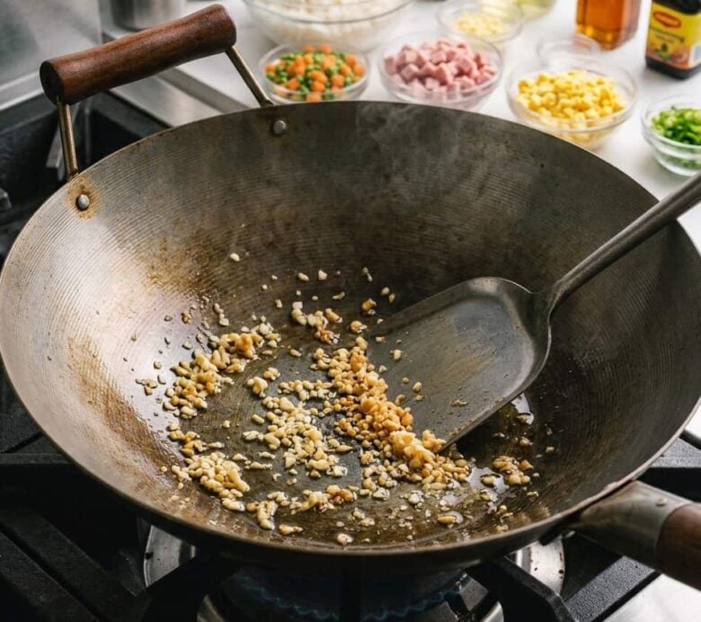Adding the oil and the minced garlic to the hot wok to cook.