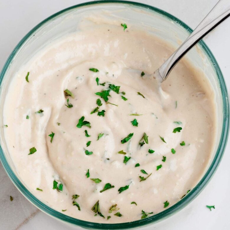 Creamy ceasar salad dressing in a clear bowl with a spoon.