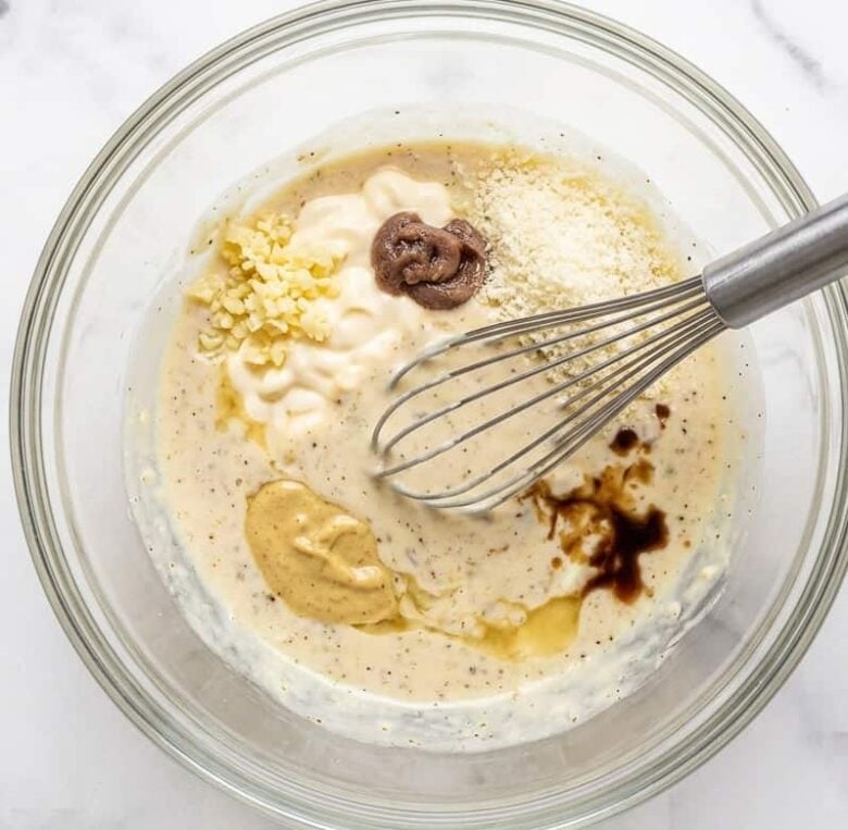 Adding all the caesar salad ingredients together into a clear bowl and using a whisk to stir.